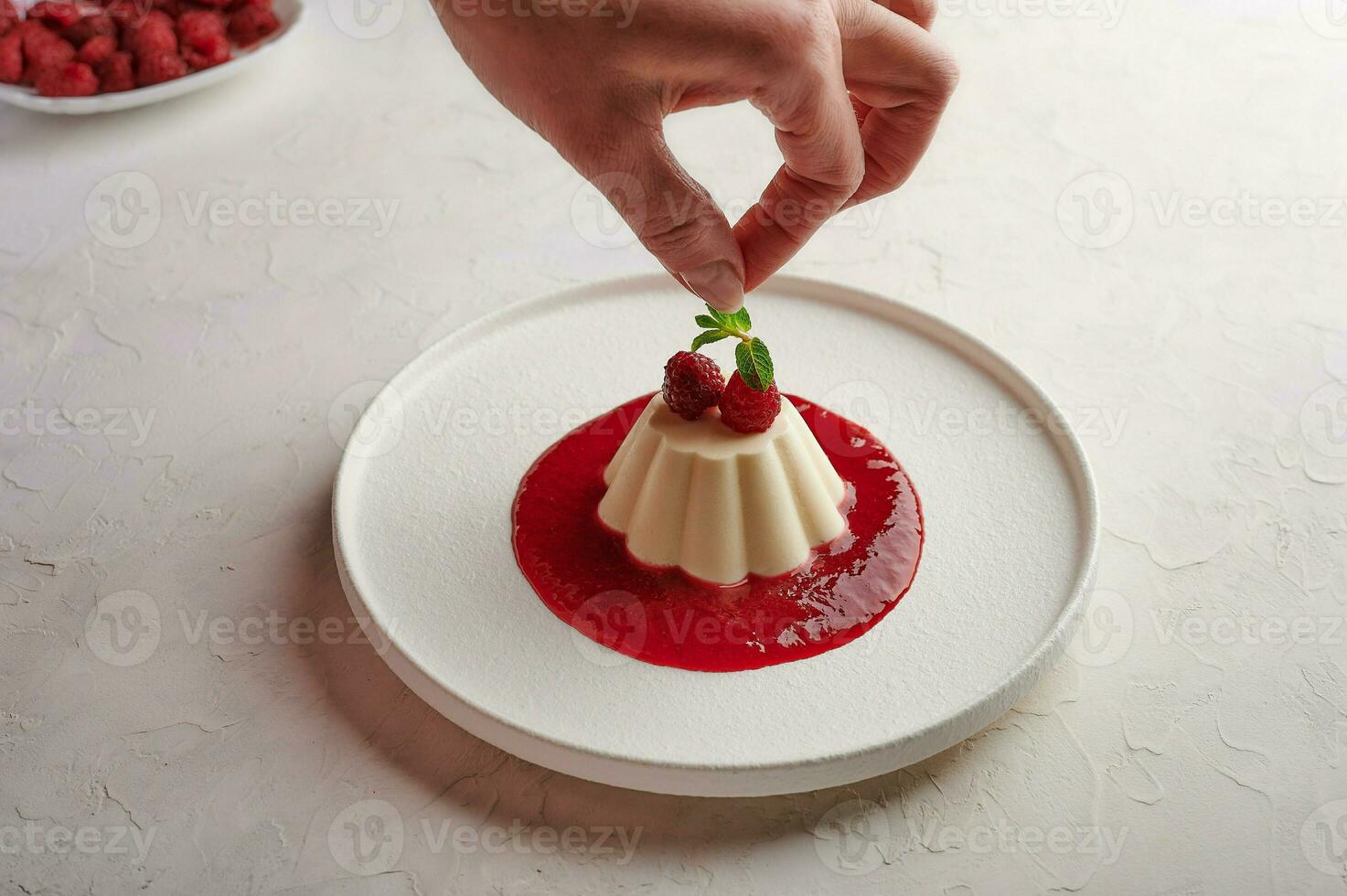 Woman's hand puts mint leaf to panna cotta with syrup and berries photo