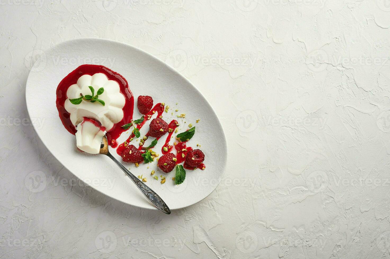 Spoon with a piece of panna cotta with syrup, raspberries and mint in oval plate, food stylind photo