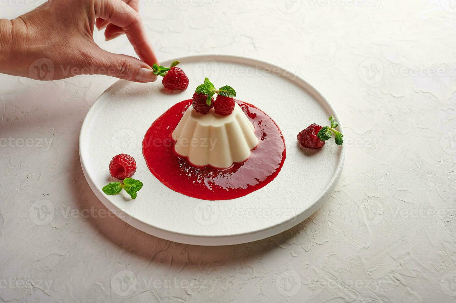 Woman's hand puts raspberry to panna cotta with syrup photo