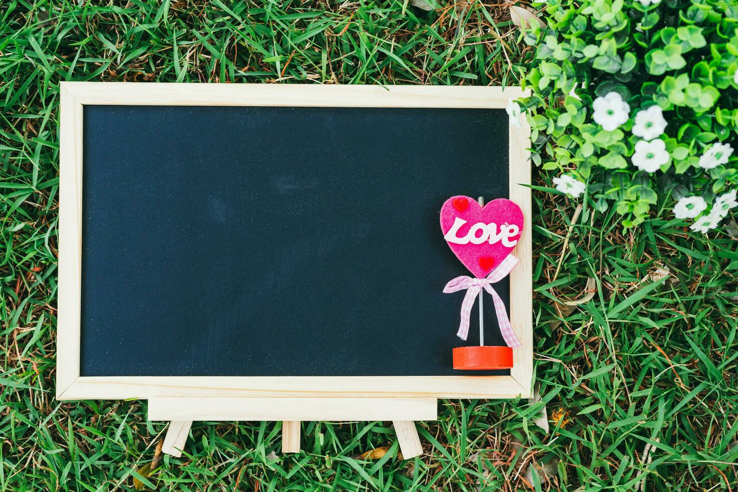 empty wooden blackboard and Flowerpot in square shape on green grass in the park background,Love concept with heart desktop. photo