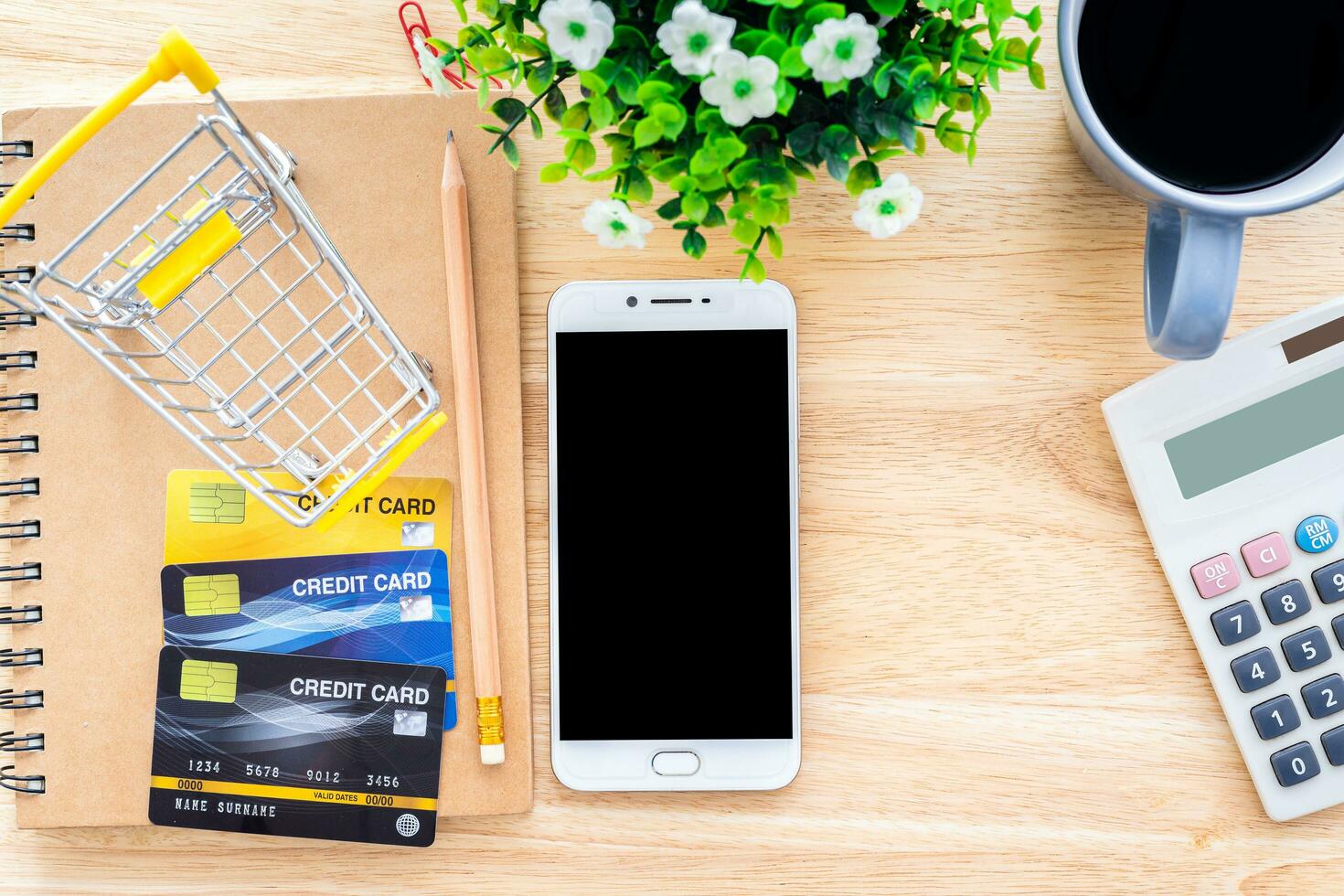 Credit cards,notebook,flower pot tree,smartphone,Shopping cart and coffee cup on wooden background,Online banking Concept,Top view office table. photo