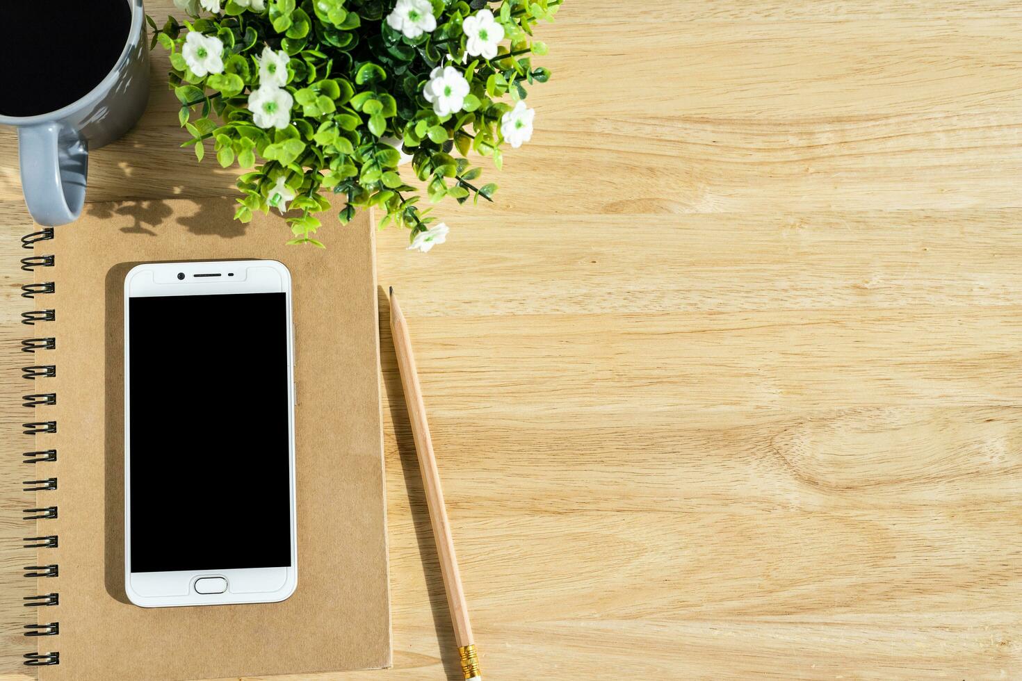 Smartphone on notebook,flower pot tree,a pencil and coffee cup on wooden background,Top view with copy space office table. photo