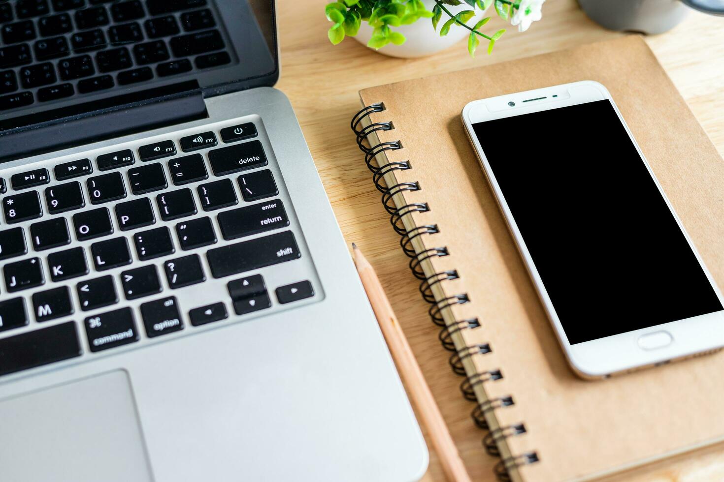 laptop with smartphone on notebook,a pencil and flower pot tree on wooden background,Top view office table. photo