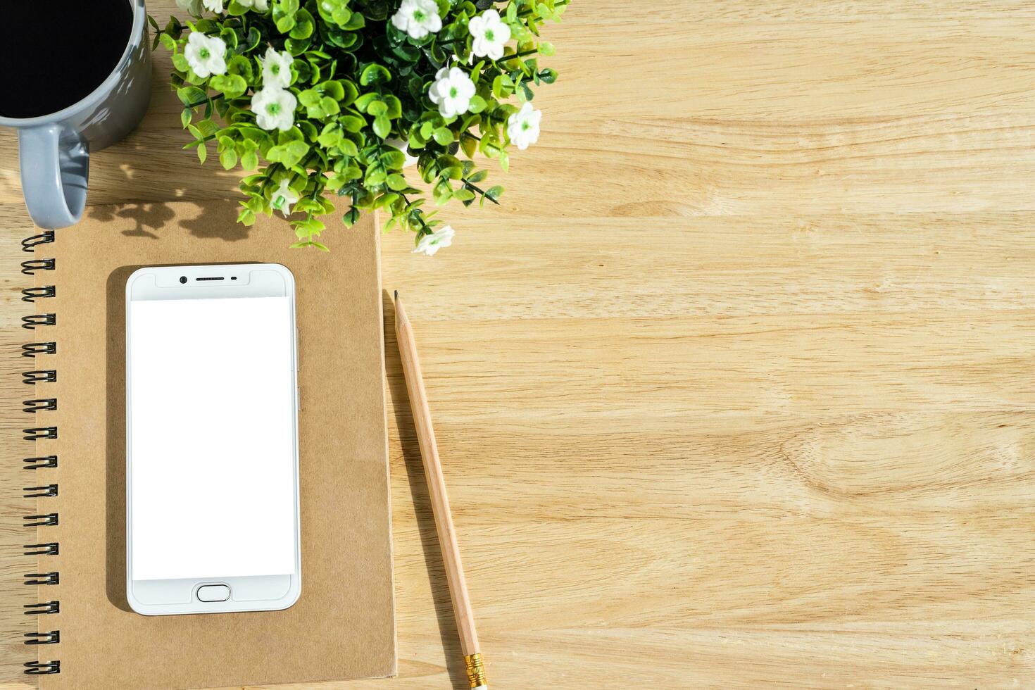 Smartphone on notebook,flower pot tree,a pencil and coffee cup on wooden background,Top view with copy space office table. photo