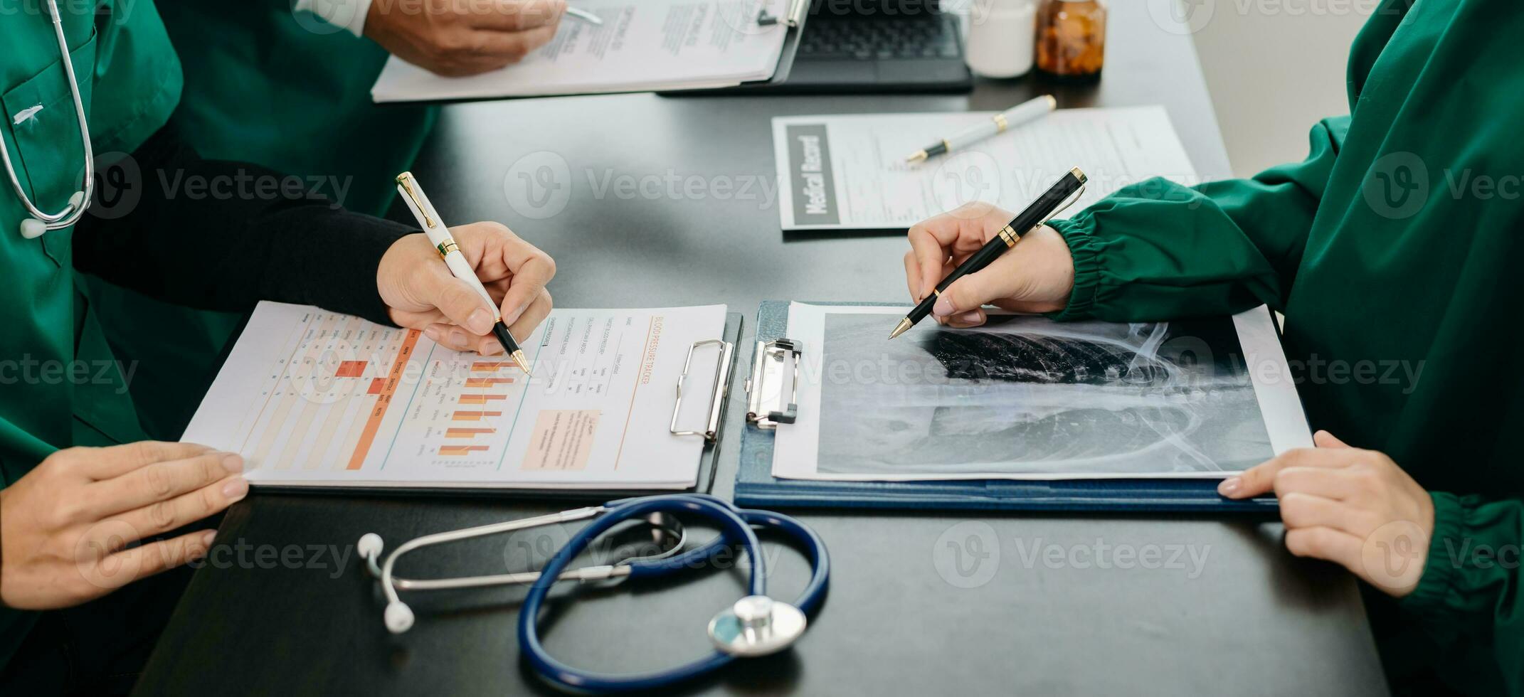 Medical team having a meeting with doctors in white lab coats and surgical scrubs seated at a table discussing a patients working online using computers in the medical photo