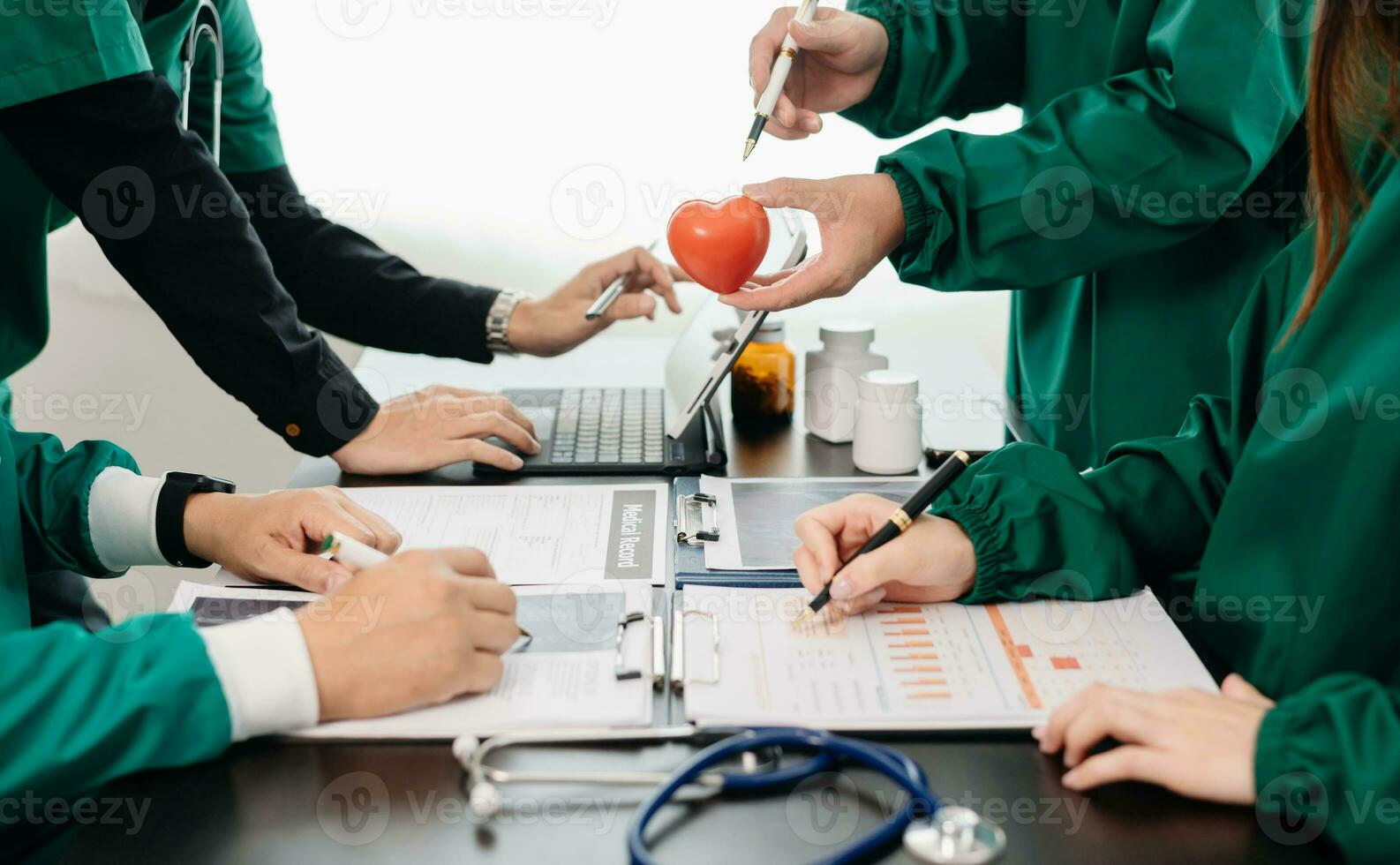 Medical team having a meeting with doctors in white lab coats and surgical scrubs seated at a table discussing a patients working online using computers in the medical photo