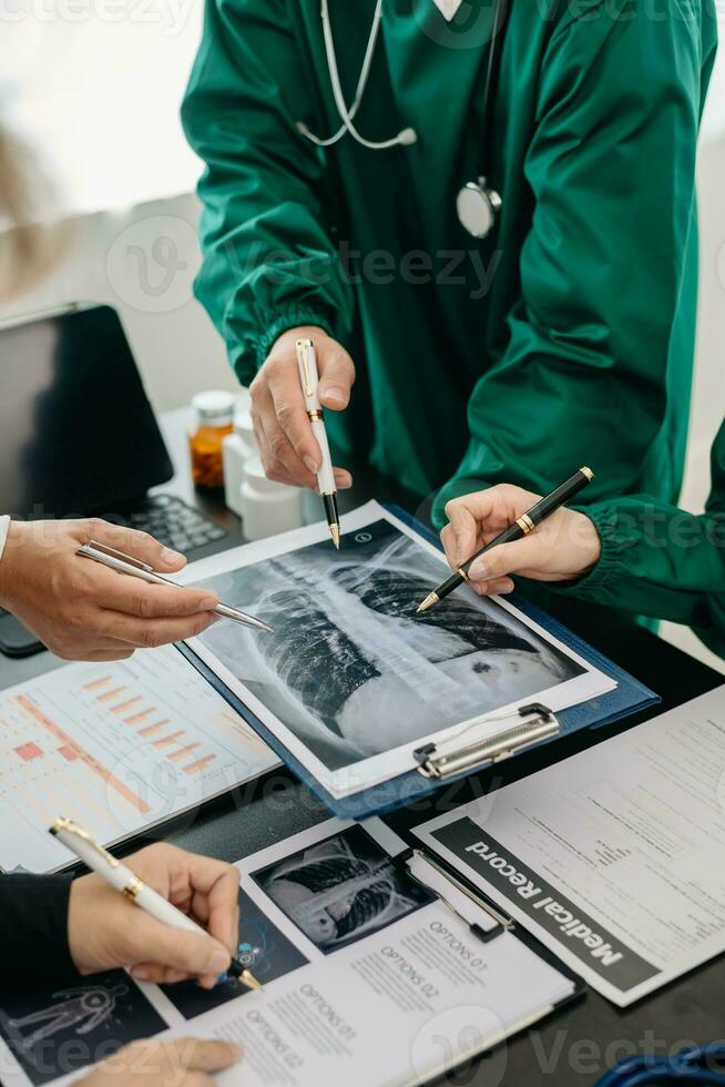 Medical team having a meeting with doctors in white lab coats and surgical scrubs seated at a table discussing a patients working online using computers in the medical photo