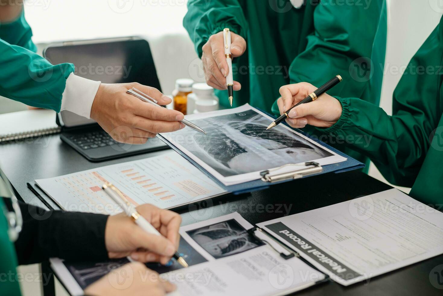 Medical team having a meeting with doctors in white lab coats and surgical scrubs seated at a table discussing a patients working online using computers in the medical photo