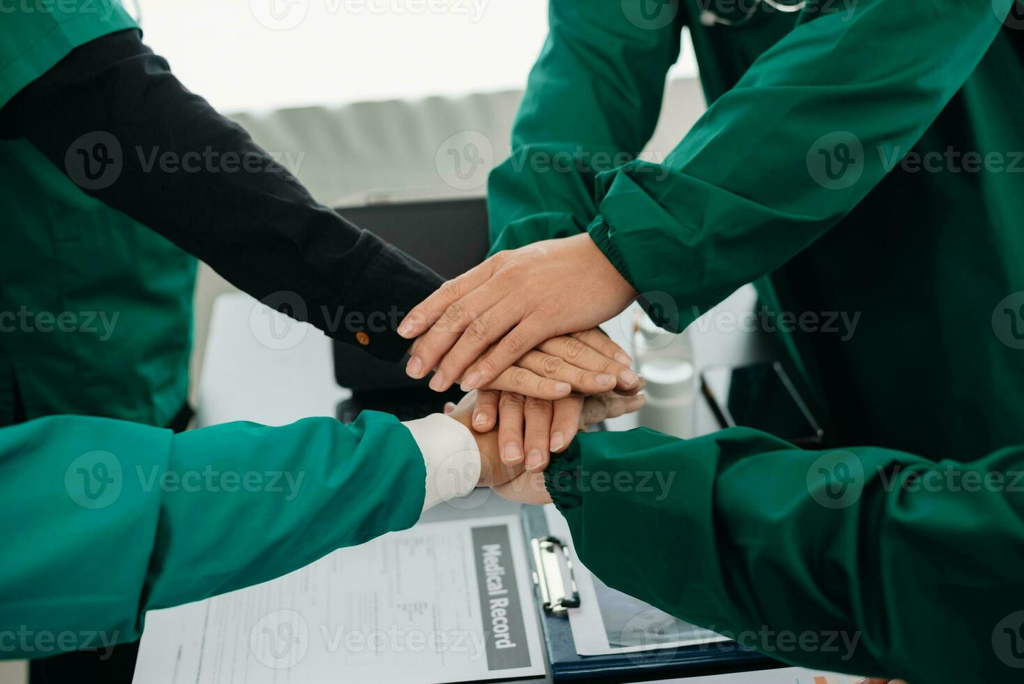 Medical team having a meeting with doctors in white lab coats and surgical scrubs seated at a table discussing a patients working online using computers in the medical photo