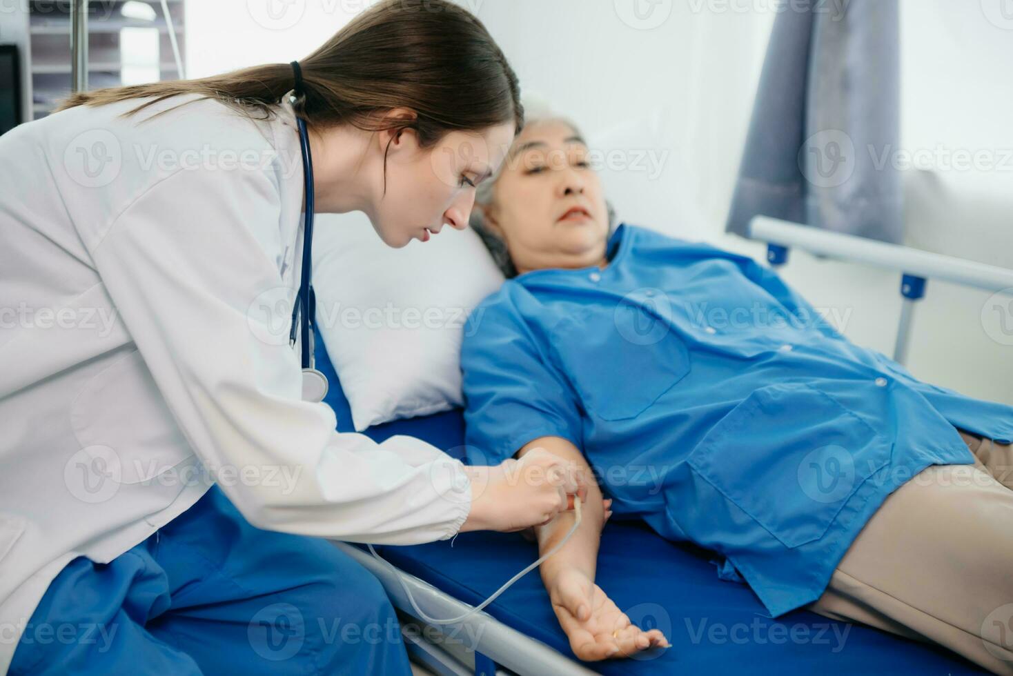 Doctor in white suit take notes while discussing and Asian elderly, woman patient who lying on bed with receiving saline solution in hospital or clinic. photo