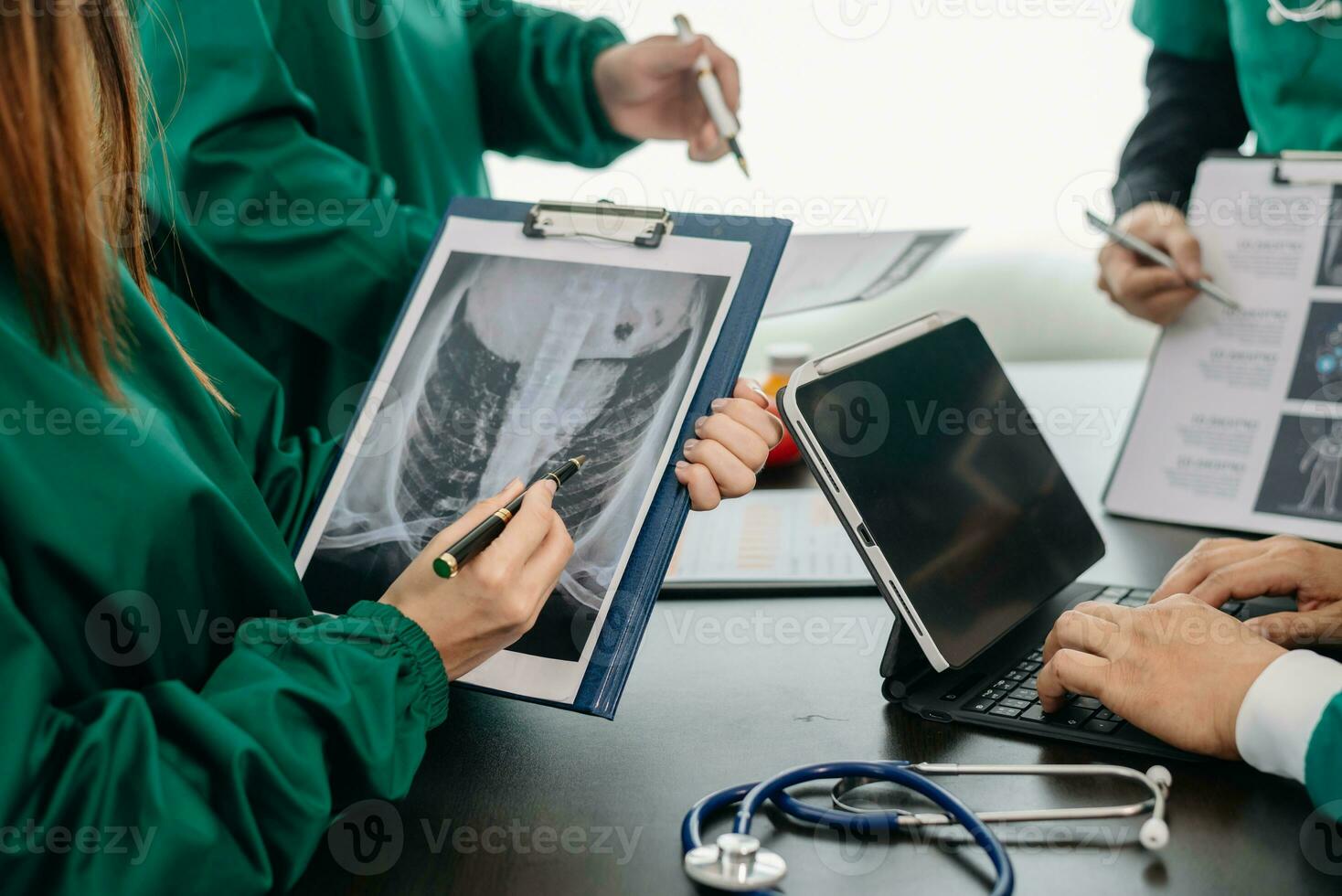 Medical team having a meeting with doctors in white lab coats and surgical scrubs seated at a table discussing a patients working online using computers in the medical photo