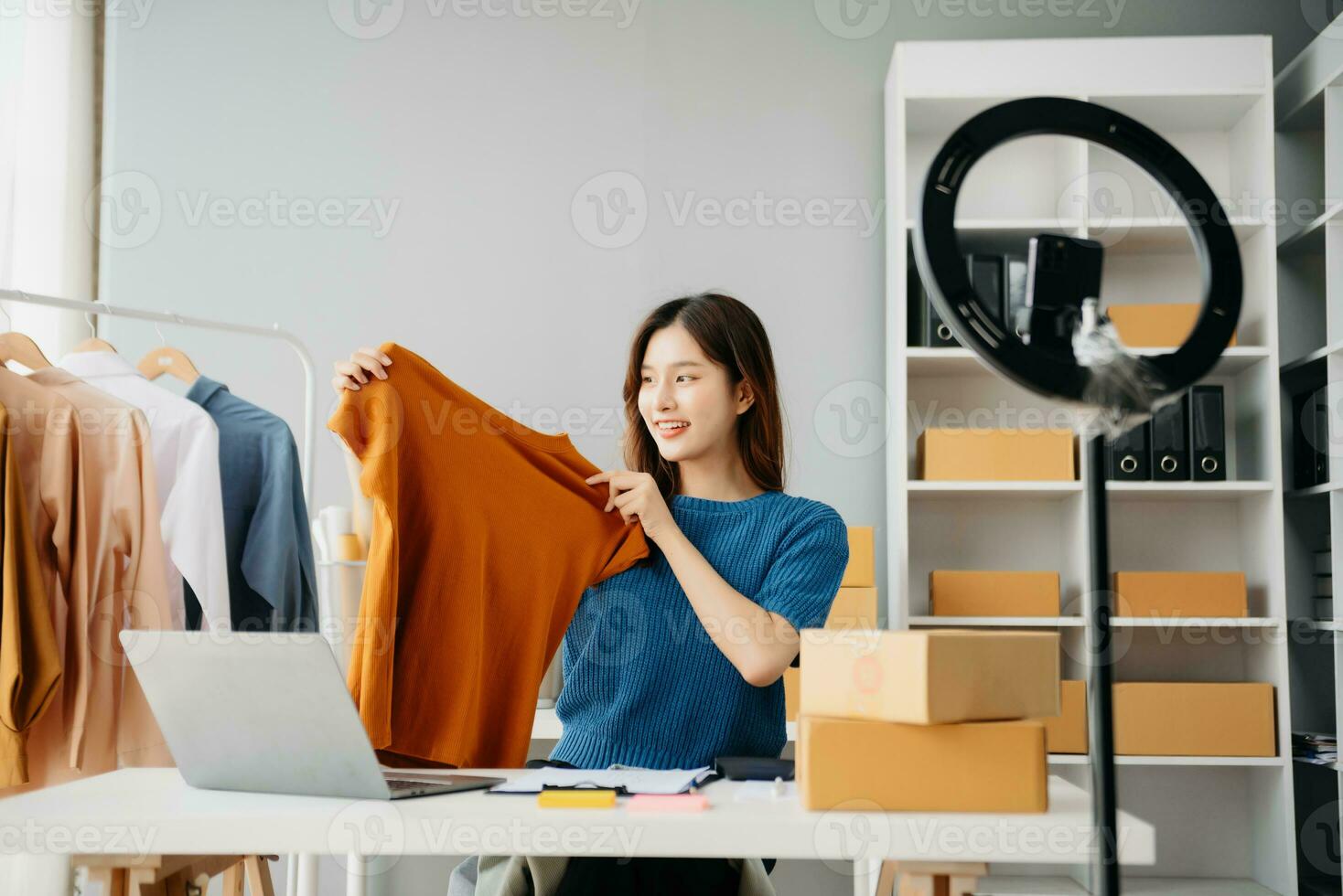 Asian lady blogger showing clothes in front of the camera to recording vlog video live streaming at her shop. photo