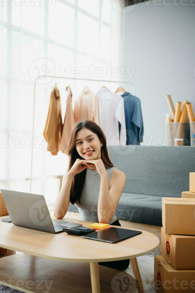 Young woman running online store Startup small business SME, using smartphone or tablet taking receive and checking online purchase shopping photo