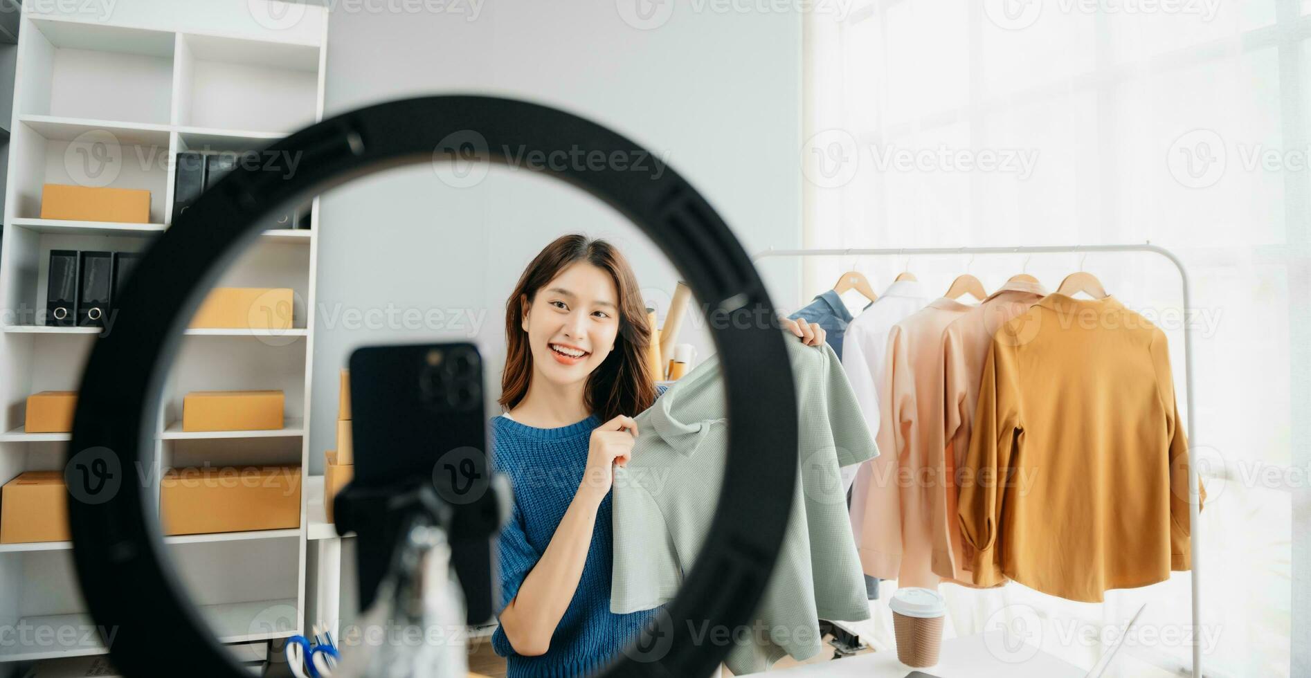 Asian lady blogger showing clothes in front of the camera to recording vlog video live streaming at her shop. photo