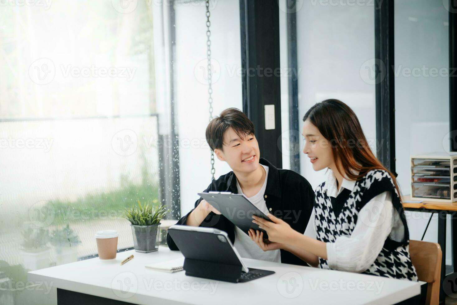 Two Asian businesswoman and man discuss investment project working and planning strategy with tablet laptop computer in office. photo
