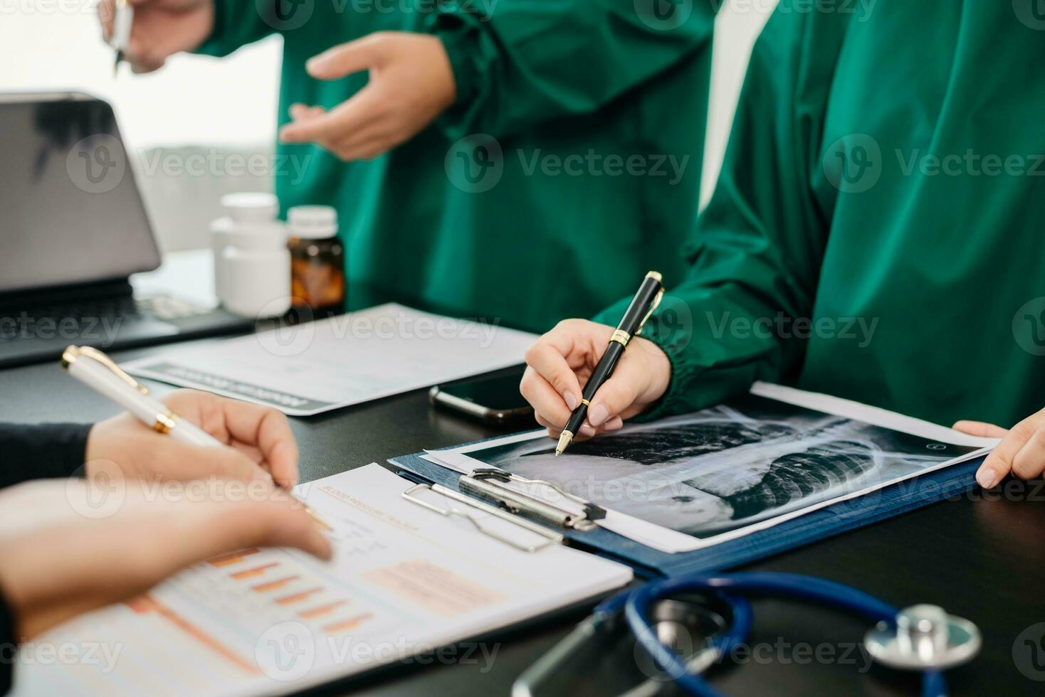 Medical team having a meeting with doctors in white lab coats and surgical scrubs seated at a table discussing a patients working online using computers in the medical photo