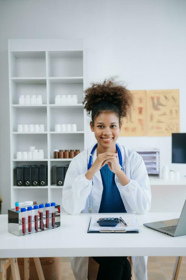 Beautiful physician doctor sit on table in office hospital. Attractive therapist female practitioner pharmacist smile and use tablet and laptop in hospital.after success work from treatment photo