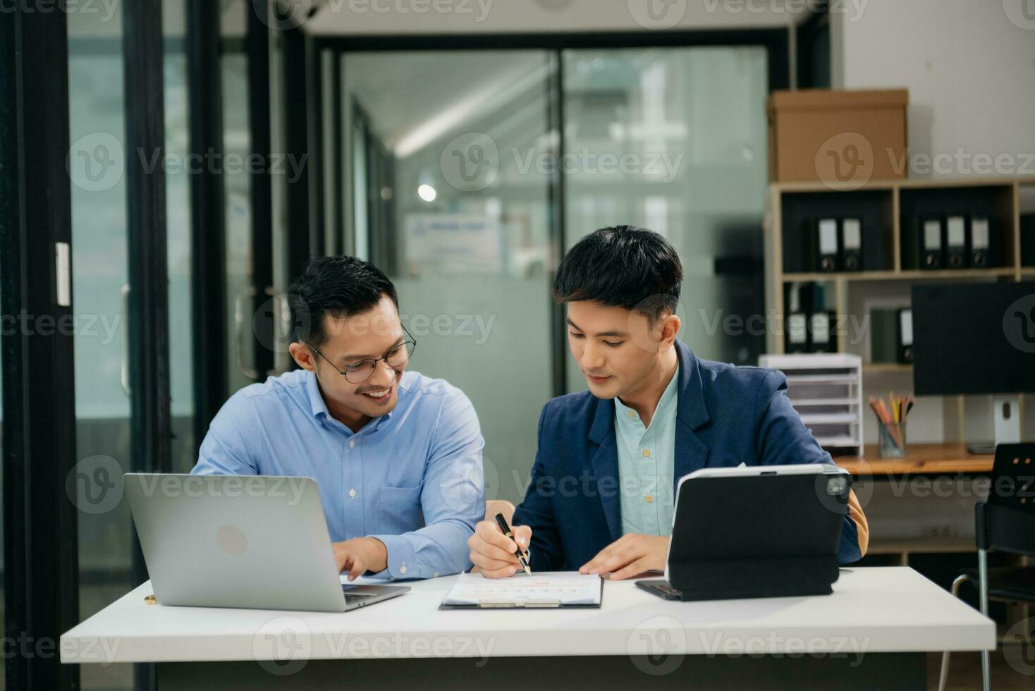 Two Asian businessman discuss investment project working and planning strategy with tablet laptop computer in modern office. photo