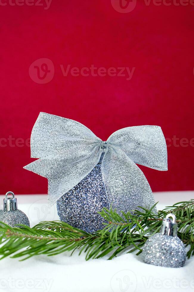 Silver Christmas balls with glitter bow and fir branch in  snow on red background. Happy New Year card. Copy space photo