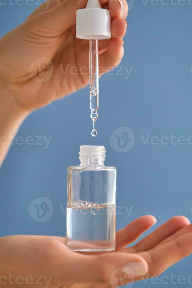 Serum with a pipette in female hands on a blue background. photo