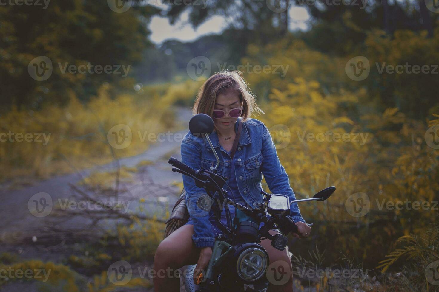 beautiful woman wearing blue jeans jacket sitting on enduro motorcycle against colorful natural  background photo