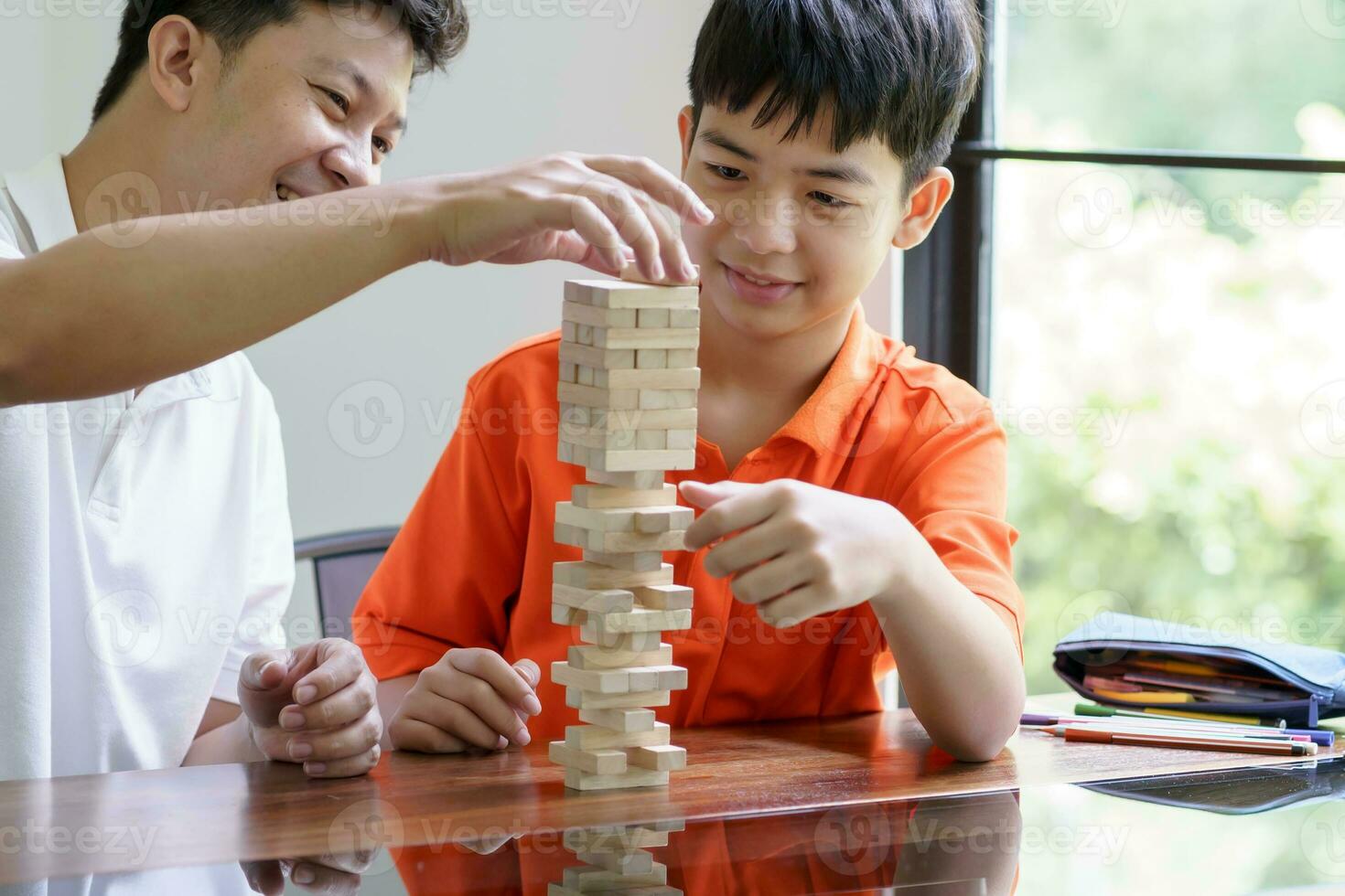 Asian father and son playing wood blocks game Carefree kid playing wood blocks game building constructor from blocks with father at home photo