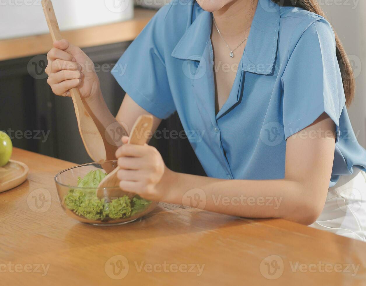A young woman with a beautiful face in a blue shirt with long hair eating fruit sitting inside the kitchen at home with a laptop and notebook for relaxation, Concept Vacation. photo