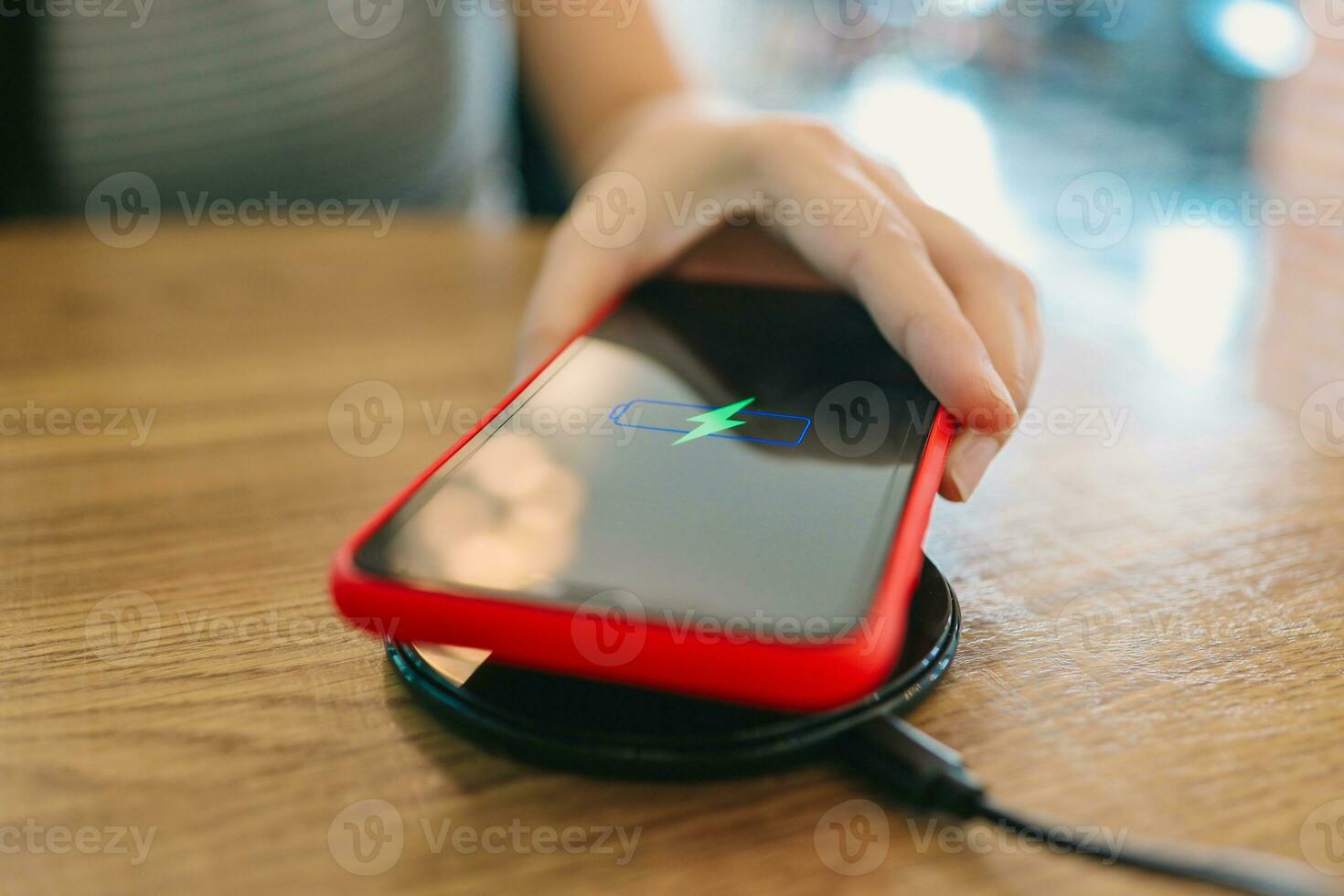 Charging mobile phone battery with wireless device in the table. Smartphone charging on a charging pad. Mobile phone near wireless charger. photo