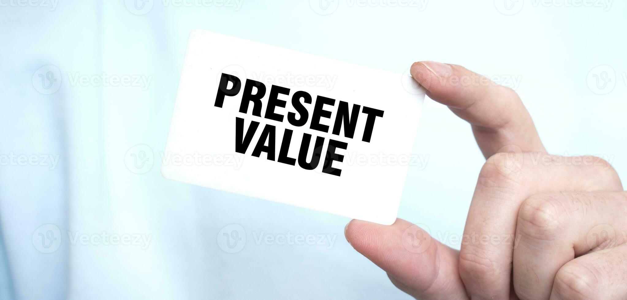 Man in blue sweatshirt holding a card with text PRESENT VALUE, business concept photo