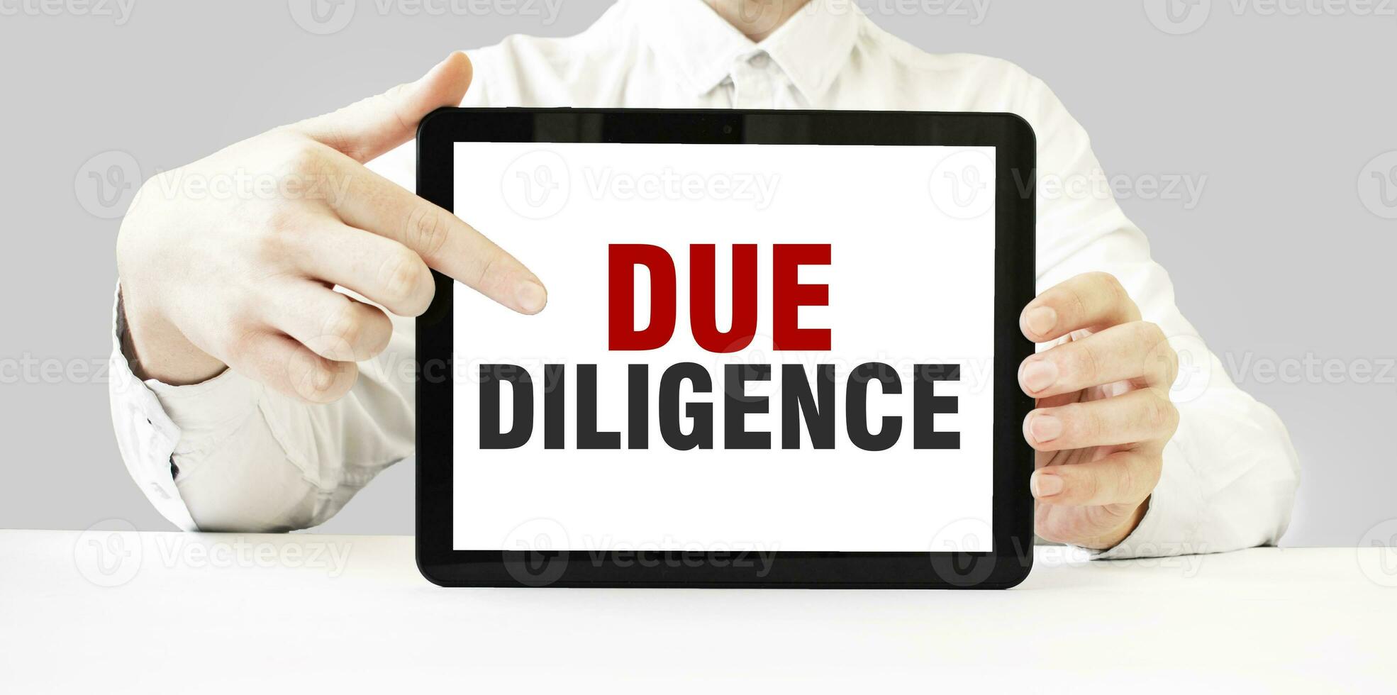 Text DUE DILIGENCE on tablet display in businessman hands on the white background. Business concept photo