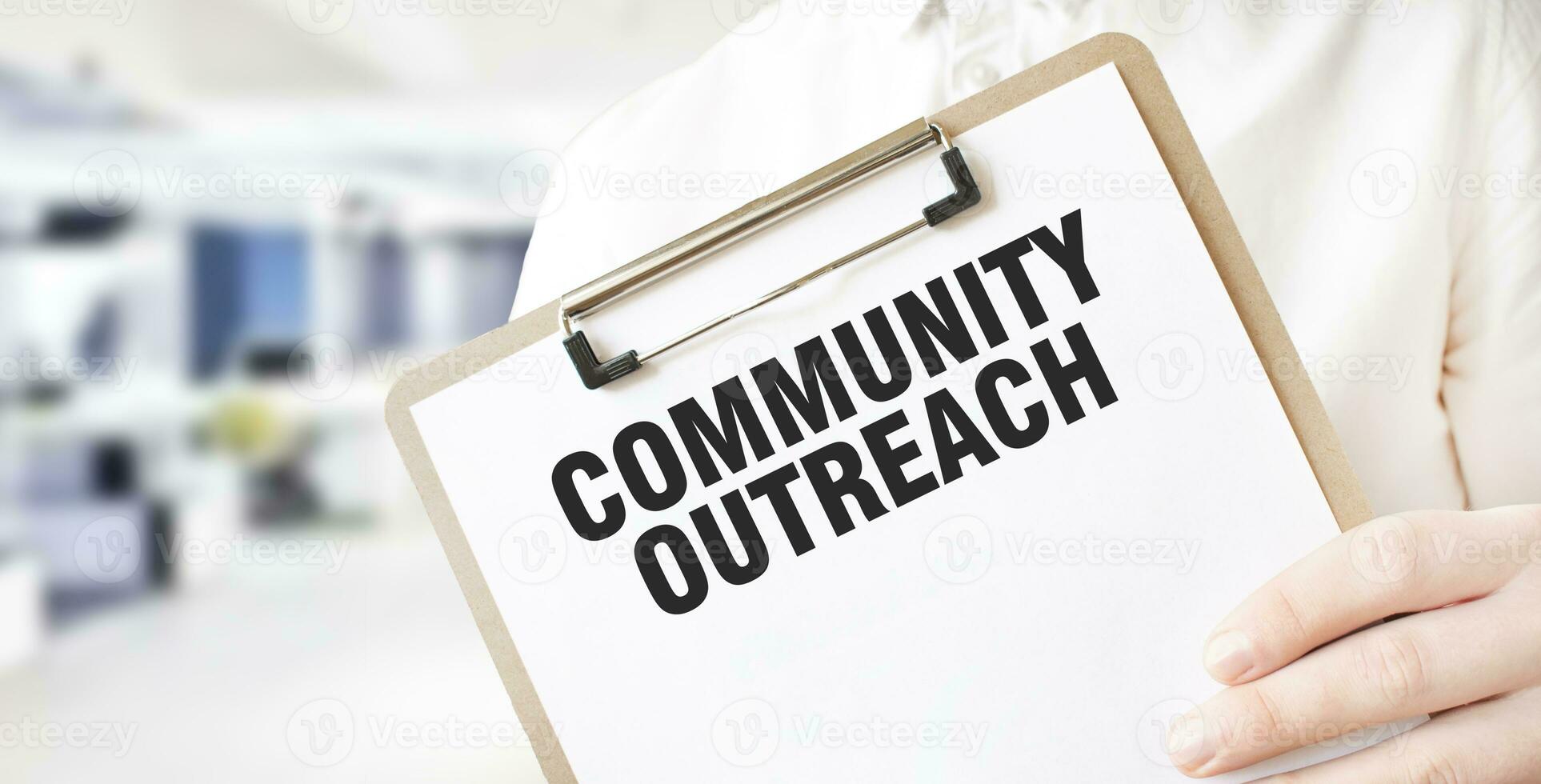 Text COMMUNITY OUTREACH on white paper plate in businessman hands in office. Business concept photo