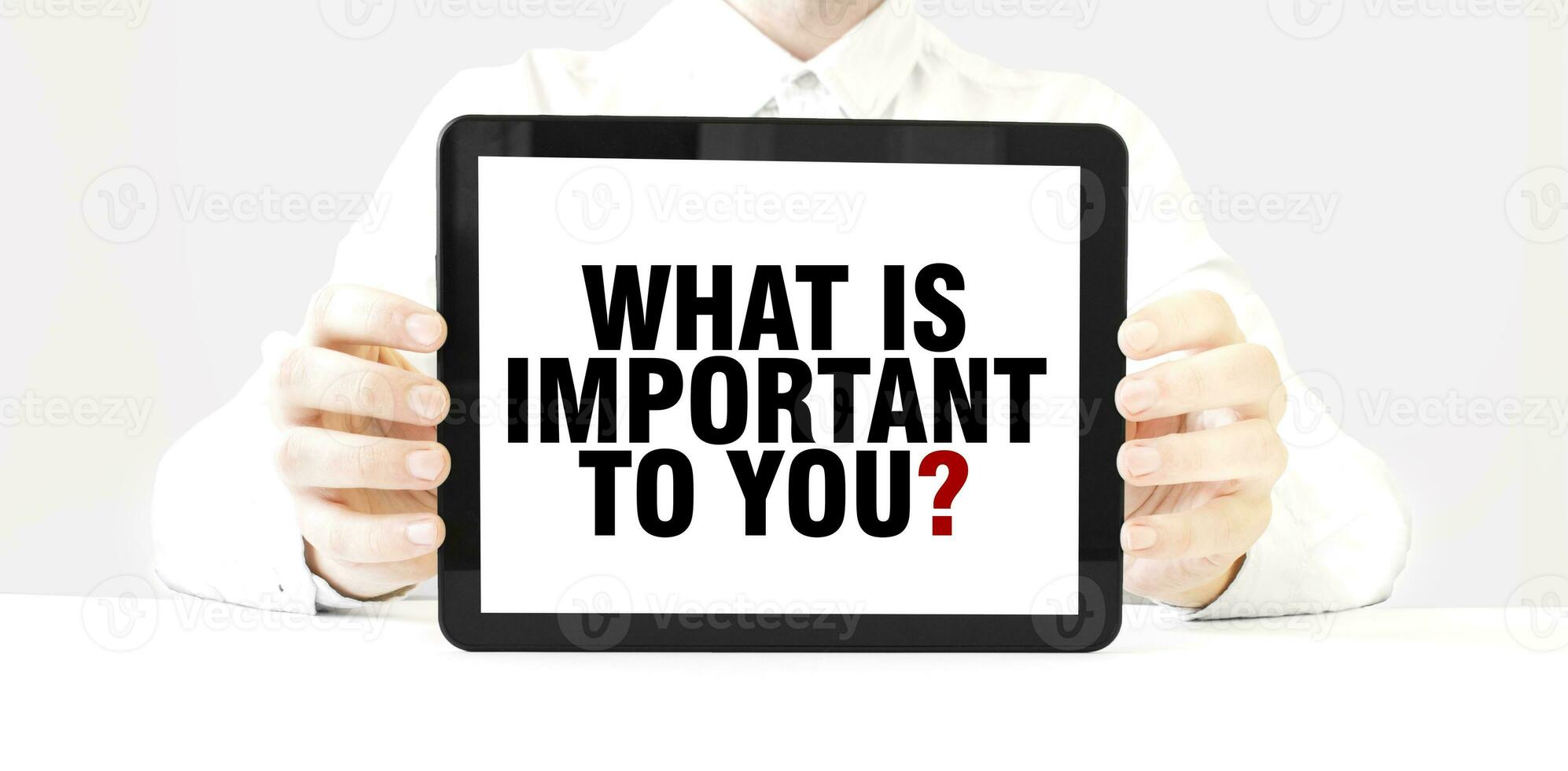 Text WHAT IS IMPORTANT TO YOU on tablet display in businessman hands on the white background. Business concept photo