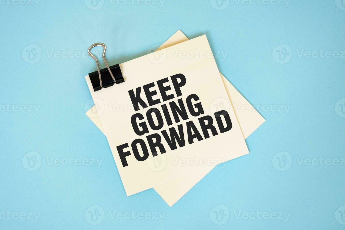 Text KEEP GOING FORWARD on sticky notes with copy space and paper clip isolated on red background.Finance and economics concept. photo