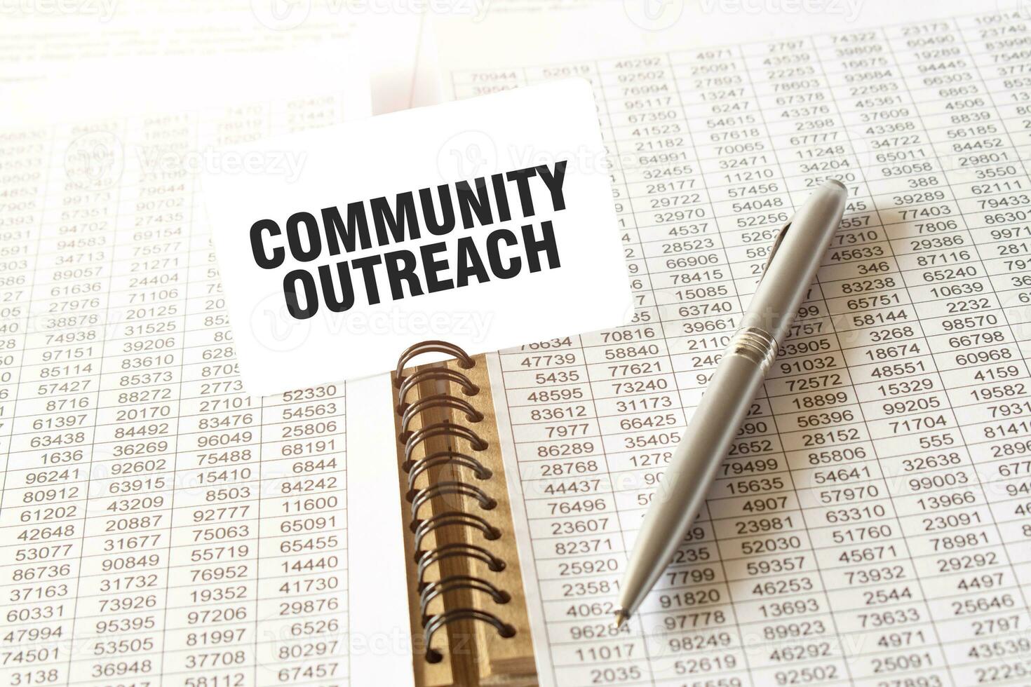 Text COMMUNITY OUTREACH on paper card, pen, financial documentation on table photo