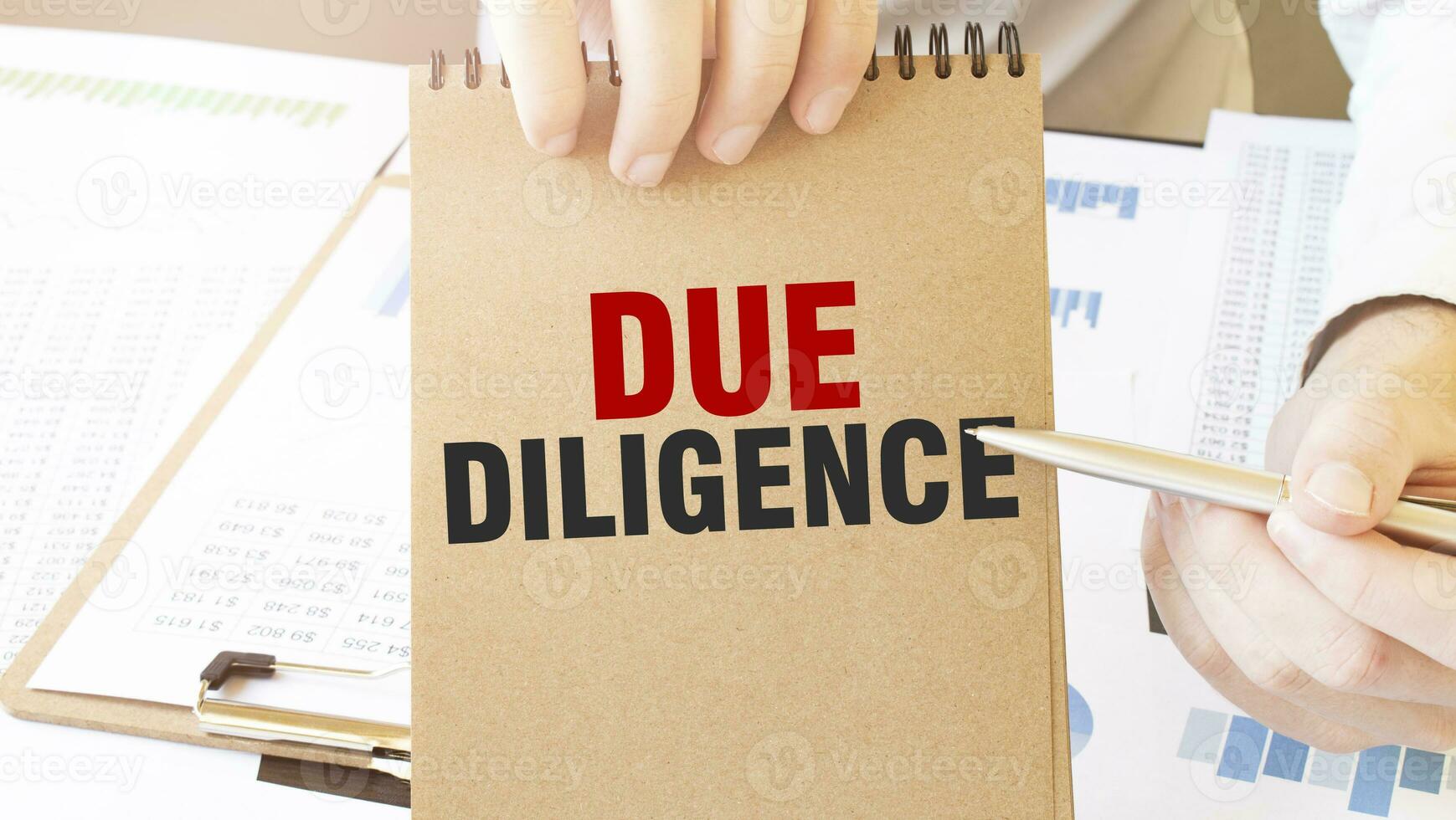 Text DUE DILIGENCE on brown paper notepad in businessman hands on the table with diagram. Business concept photo