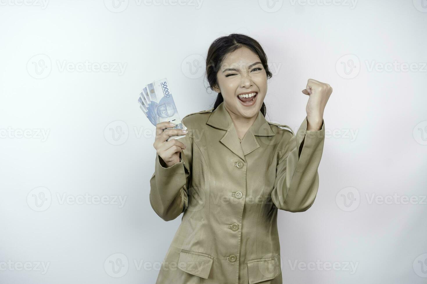 A successful young government worker woman is wearing khaki uniform holding cash money in Indonesian rupiah isolated by white background photo