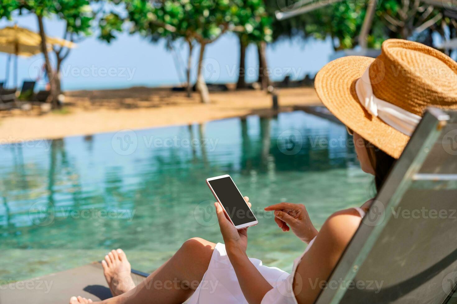 Young woman traveler relaxing and using a mobile phone by a resort pool while traveling for summer vacation, Travel lifestyle concept photo