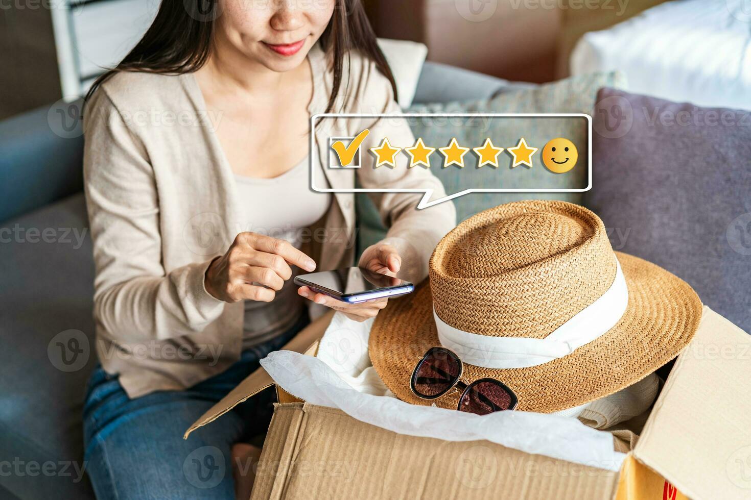 Young happy woman using smartphone to give a five-star satisfaction rating and unpacking parcel online shopping order at home photo