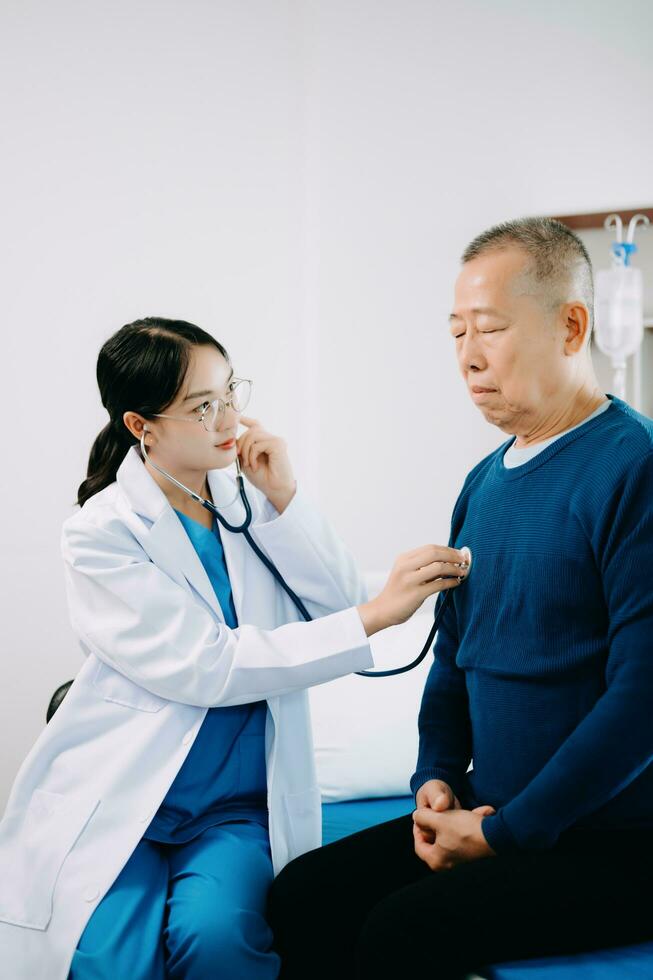 Asian doctor in white suit take notes while discussing and Asian elderly, man patient who lying on bed with receiving saline solution in hospital photo