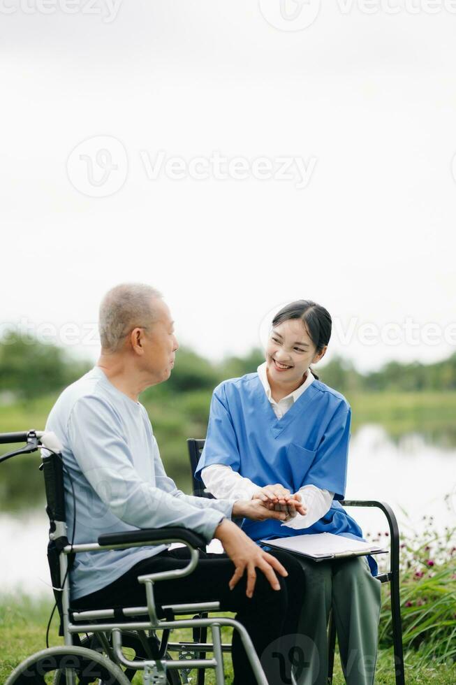mayor asiático mayor hombre en silla de ruedas con asiático Cuidado cuidador enfermería hogar hospital jardín concepto son caminando en el jardín. a ayuda y alentar. foto