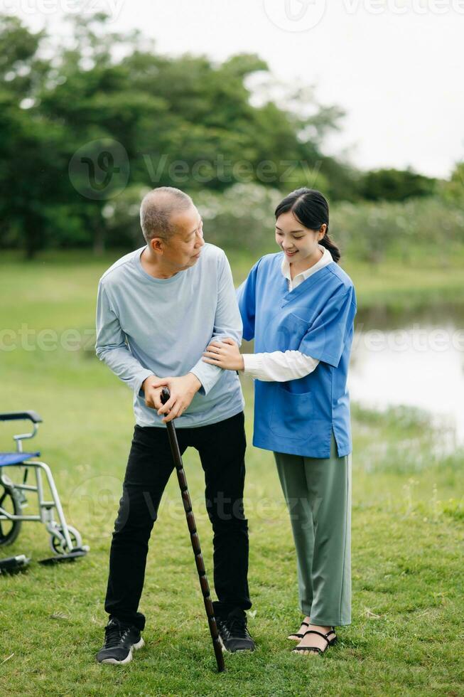 Elderly asian senior man on wheelchair with Asian careful caregiver. Nursing home hospital garden concept. photo