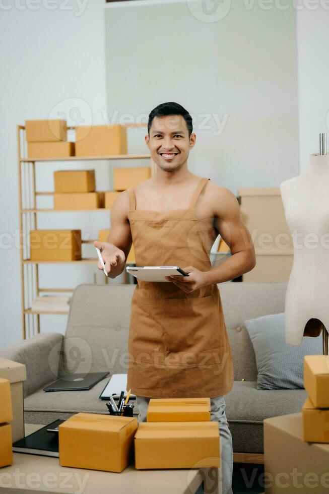 Startup small business SME, Entrepreneur owner man using smartphone or tablet taking receive and checking online purchase shopping order to preparing pack product box. photo