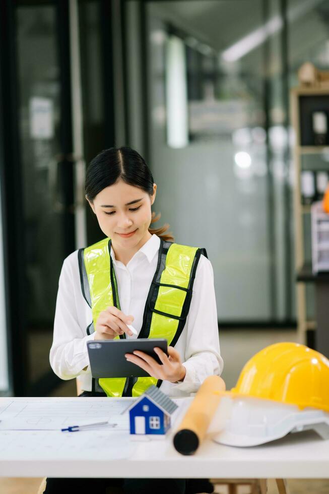 Creative architect projecting on the big drawings working and laptop with on on architectural project at construction at desk in office. Asian woman industry professional photo