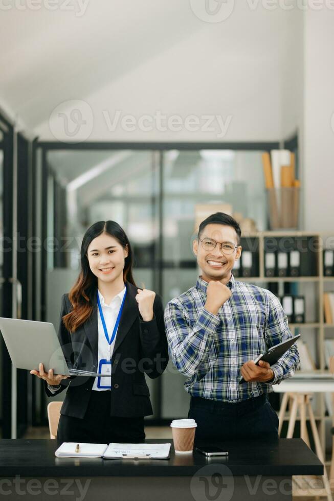 Asian business colleague business presents and explains and using laptop and tablet. Teamwork, financial marketing team, while sitting in modern office photo