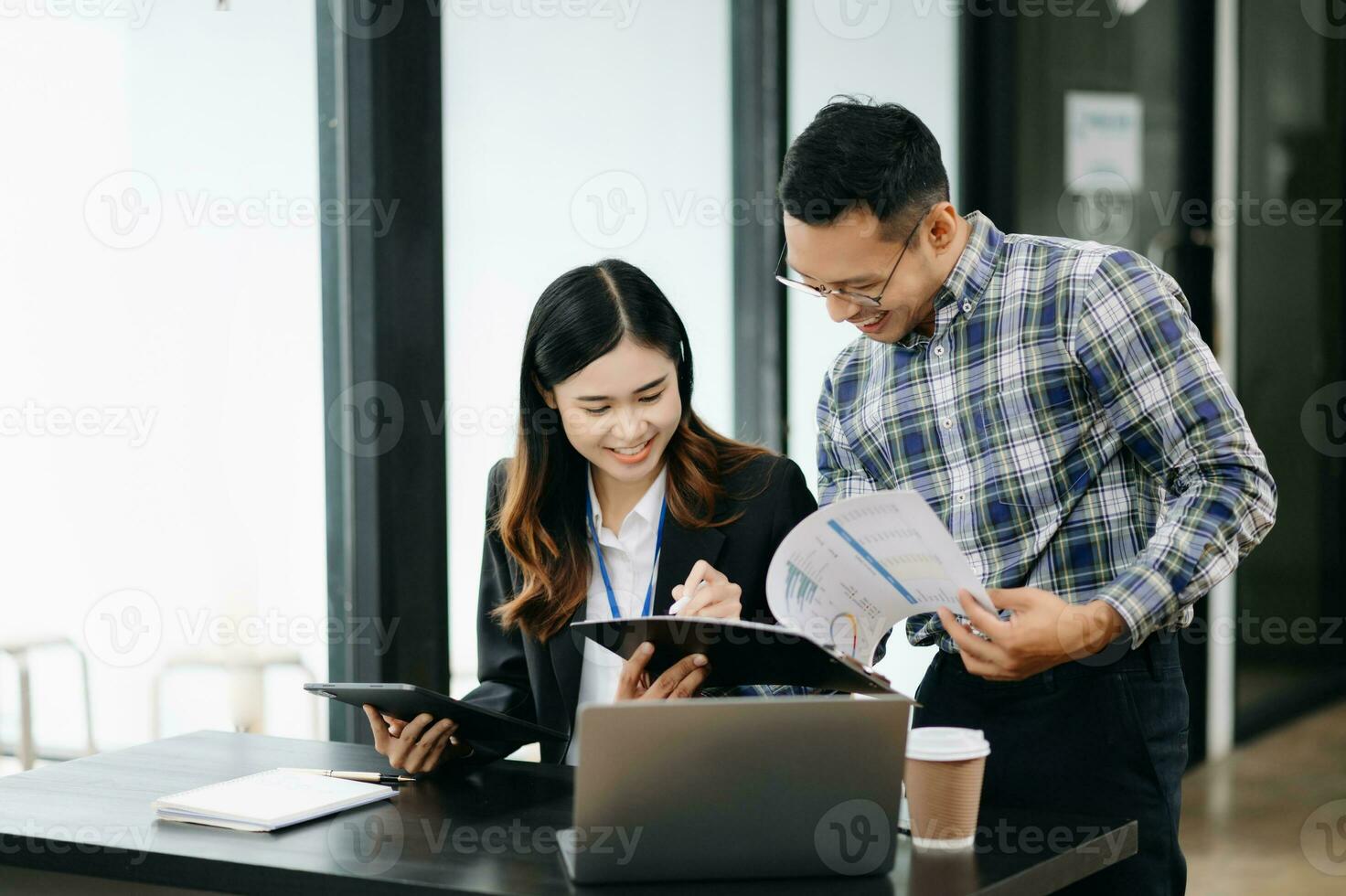 Asian business colleague business presents and explains and using laptop and tablet. Teamwork, financial marketing team, while sitting in modern office photo