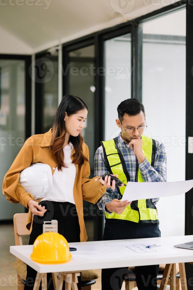 Engineer teams meeting working together wear worker helmets hardhat with on architectural project site and making model house. Asian industry professional team in office photo