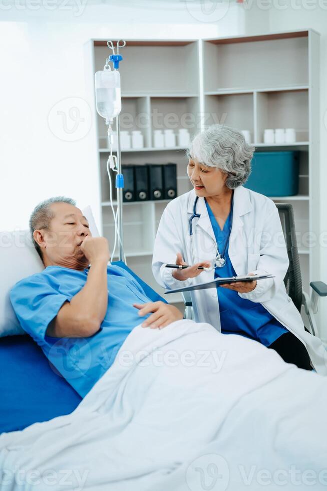 Friendly Female Head Nurse Making Rounds does Checkup on Patient Resting in Bed. She Checks tablet while Man Fully Recovering after Successful Surgery in hospital photo