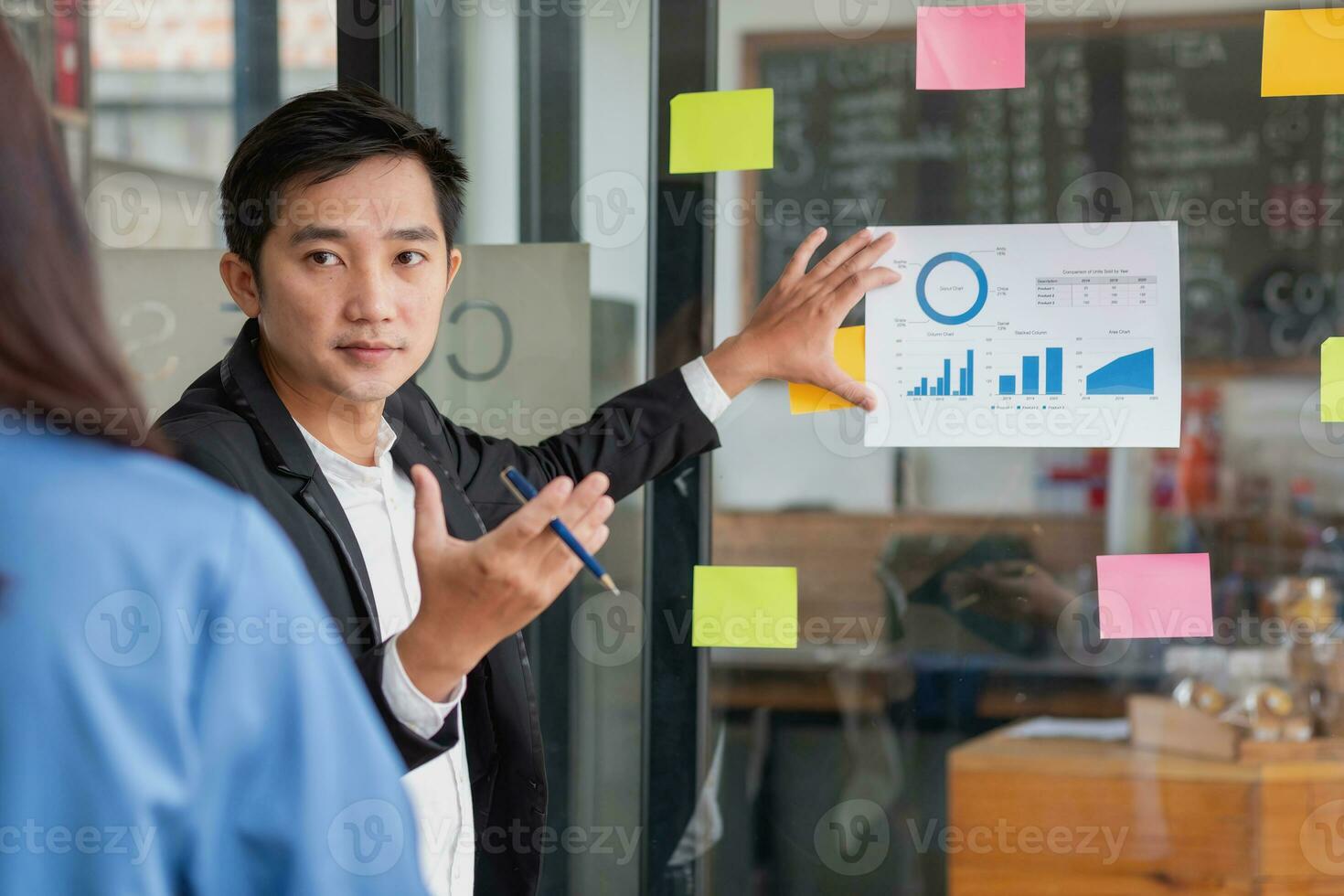 A man employee writes on a colorful notepad. Ethnic women working at startups brainstorm collaborative plans on glass wall stickers See less. photo