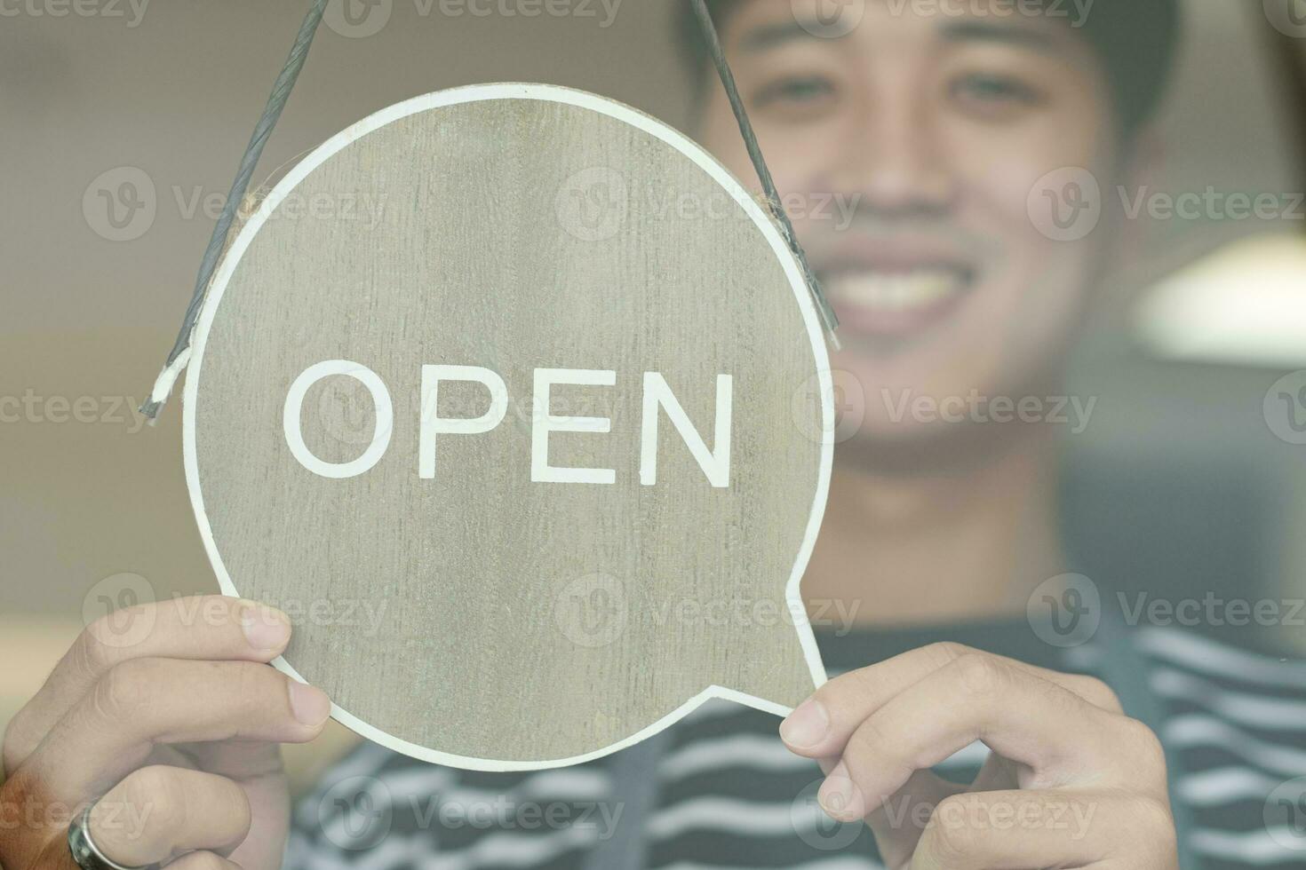 Happy Coffee Shop owner in an apron turning open sign board on glass door. Small business owner opening a small business. photo