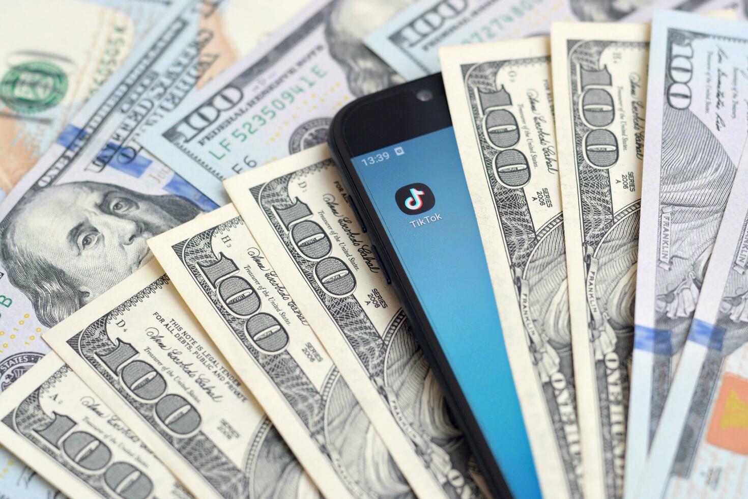 Smartphone screen with Tiktok app and lot of hundred dollar bills. Business and social networking concept photo